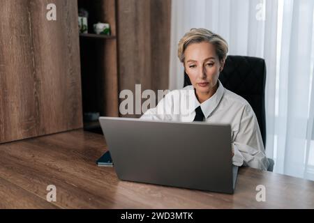 Attractive thoughtful concerned middle-aged adult 50s woman working on laptop computer in office looking to screen, thinking solving problem. Stock Photo
