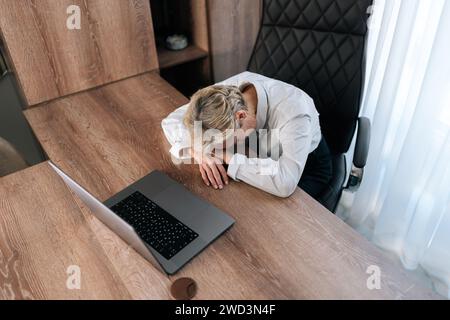 Top view of exhausted female entrepreneur fall asleep on desk overwhelmed with computer work at office. Tired middle-aged business woman sleep Stock Photo