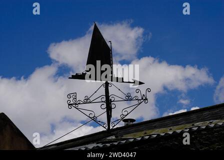 Weather vane in form of sailing boat with mainsail hoisted seen in silhouette against blue sky and puffy white clouds Stock Photo