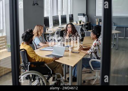 Three multi-ethnic women and indian man in wheelchair having business meeting at desk in office Stock Photo
