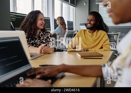 Biracial colleagues smiling at each other while having conversation at desk during workday in office Stock Photo
