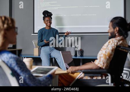 Joyful black employee giving presentation with code on digital board, her coworkers listening to her Stock Photo
