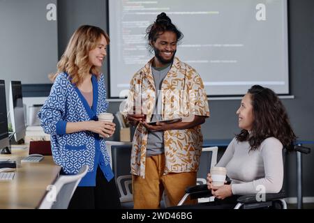 Caucasian woman and indian man smiling at their colleague in wheelchair during coffee break at work Stock Photo