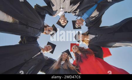 College graduates in a circle stand hugging each other. Stock Photo