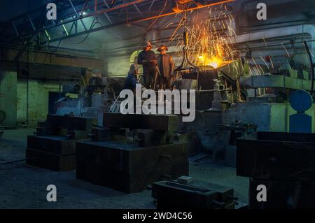Industrial workers team pouring molten metal at foundry. Steel mill laborers handling manufacturing process in workshop. Heavy industry, metallurgy Stock Photo