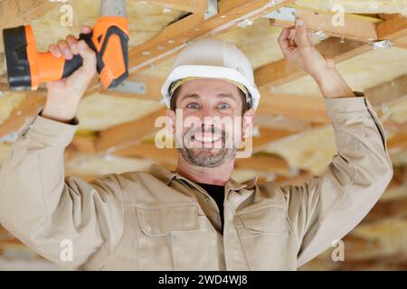 smiling handyman using cordless drill to the ceiling Stock Photo