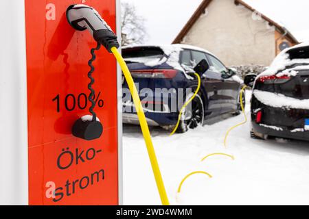 An electric car is charged with a charging cable at an electric vehicle charging station in a winter scene in Germany. The cable plug is the charging Stock Photo