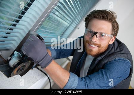 man fixing metal frame using angle grinder on windows Stock Photo