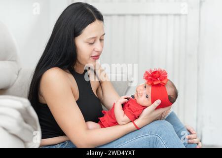 young latina mother holding her baby on her lap while looking at her with pride and love Stock Photo