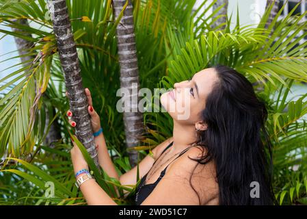 Portrait of beautiful young woman, with black hair, among leaves and branches of green plants posing for a photo. Person traveling. Stock Photo