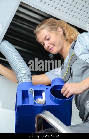 happy female worker fitting ventilation system in buildings ceiling Stock Photo