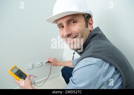 happy electrician checking voltage in electrical wall socket Stock Photo