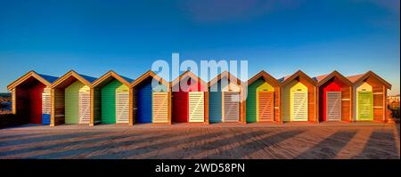 Panoramic view of the colourful beach huts on blyth promenade at dawn in northumberland with a clear blue sky behind Stock Photo