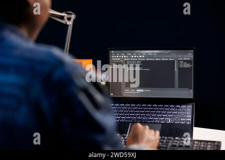 African American developer managing a system, typing on keyboard and laptop screen showing software programming. Professional freelancer working on data center and network security. Stock Photo