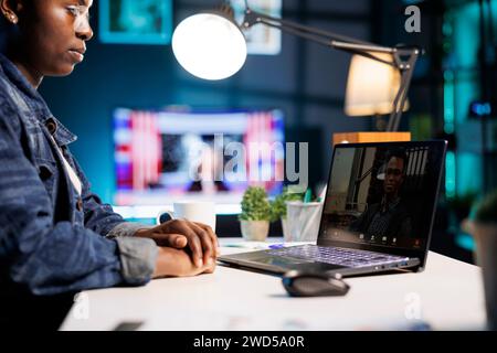 Close-up of african american freelancer sitting at table at home having video conference with male colleague. Female college student studying online with laptop, virtual communication with professor. Stock Photo