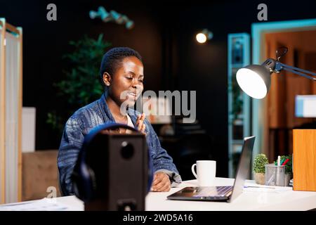 Young black woman waving at laptop camera, attending online class, virtual communication with colleagues. African american female freelancer video conferencing with potential clients. Stock Photo