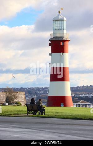 A couple seated on a public bench at West Hoe enjoying winter sunshine and the views of Smeaton’s Tower and Plymouth Sound, December 2023. Stock Photo