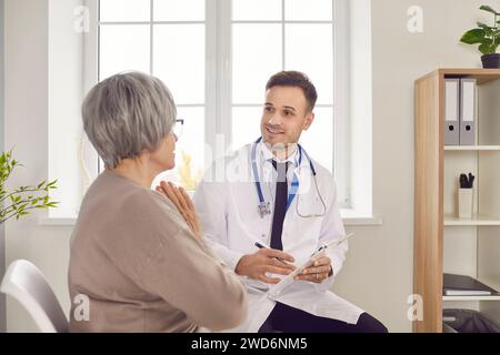 Young smiling doctor, male nurse taking care of old woman listening during check, examination Stock Photo
