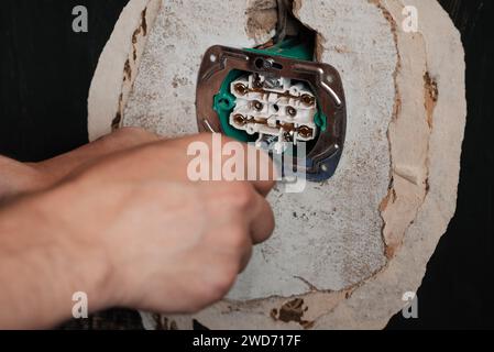 Replacing and installing a new electrical outlet. Hands with a screwdriver man electrician on the background of the wall in the house Stock Photo