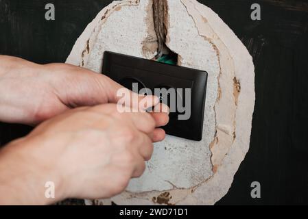 Replacing and installing a new electrical outlet. Hands with a screwdriver man electrician on the background of the wall in the house Stock Photo