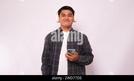 Asian young man listening music on smartphone using headphone wireless against white background Stock Photo