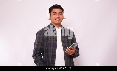 Asian young man listening music on smartphone using headphone wireless against white background Stock Photo