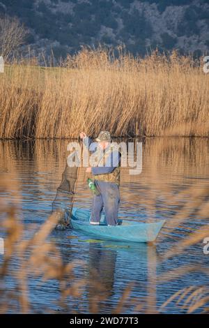 A man fishing in river, capturing fish with a net from the boat in ...