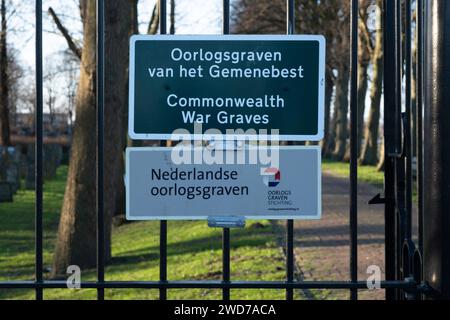 Commonwealth War Graves Cemetery sign, with English and Dutch text. Behind the fence the gravestones Stock Photo