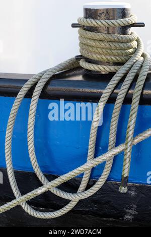Ship's ropes twisted around the iron bollard on the railing of a metal sailboat. Isolated on white background Stock Photo