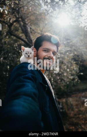 White kitten with blue eyes sitting on man shoulder Stock Photo