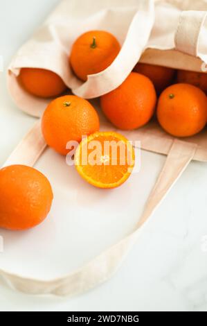 Cut mandarin orange beside a cloth bag full of mandarins Stock Photo