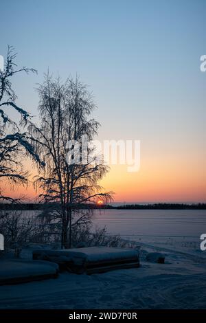 Sunset over the frozen lake in winter with snow covered trees. Stock Photo