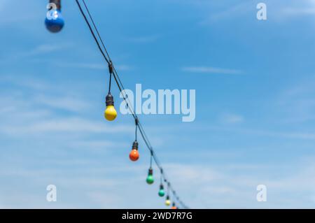 Colorful string lights for party decoration against blue sky. Vintage lightbulbs hanging on string. Stock Photo