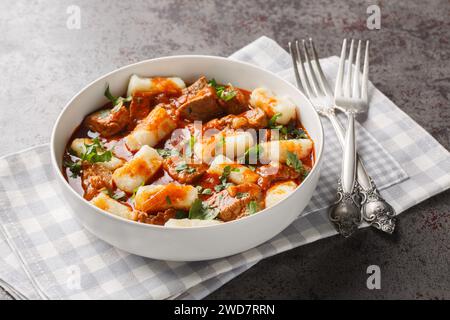 Kopytka Polish dumplings or little hooves made of mashed potatoes served with meat with gravy close-up in a plate on the table. Horizontal Stock Photo