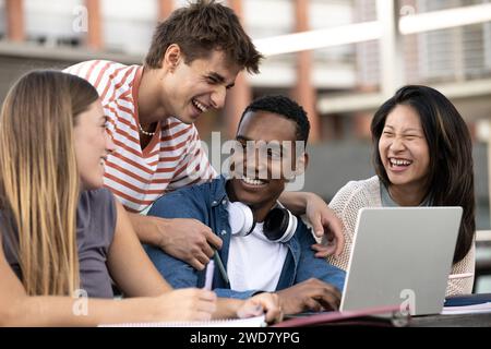 Multicultural group of people working together with a laptop.Young happy friends laughing outside using computer and notes. Stock Photo