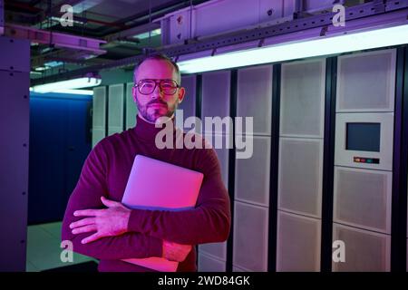 attractive focused professional in turtleneck with glasses holding laptop and looking at camera Stock Photo