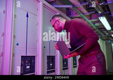 handsome focused data center specialist holding his laptop while working hard, information Stock Photo