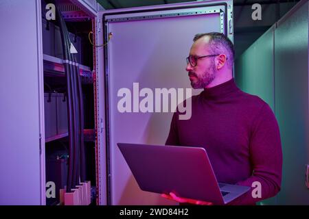 attractive concentrated specialist in turtleneck with glasses holding laptop while working hard Stock Photo