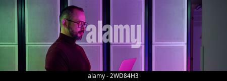 jolly professional in turtleneck with glasses and beard working on laptop, data center, banner Stock Photo