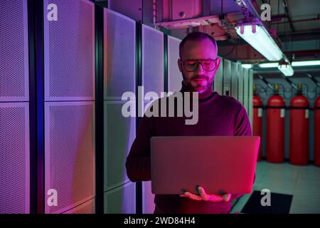 joyous attractive professional in turtleneck looking at his laptop and smiling happily, data center Stock Photo