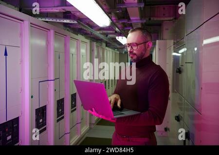 attractive focused specialist in turtleneck with glasses and beard working on his laptop, data Stock Photo