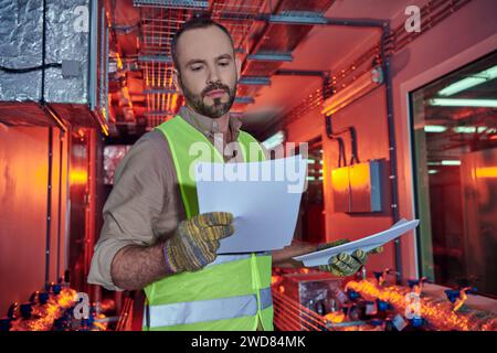 focused hardworking specialist in safety clothes looking attentively at his paperwork, data center Stock Photo