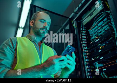 good looking bearded specialist in safety vest looking at his mobile phone, data storage Stock Photo