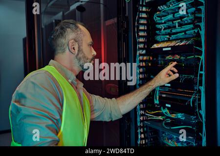 good looking pensive professional with beard in yellow safety vest inspecting data storage Stock Photo