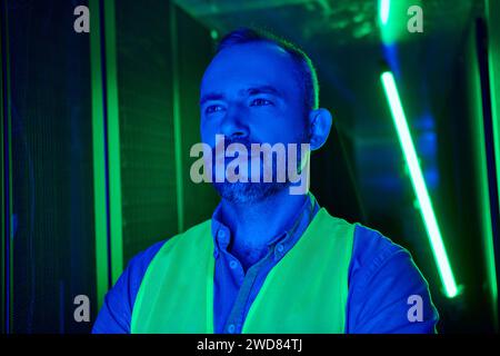 good looking bearded technician in safety vest looking away during his inspection, data center Stock Photo