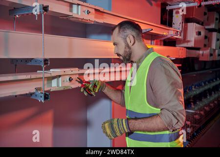 good looking pensive technician in safety vest and gloves working with pliers in data center Stock Photo