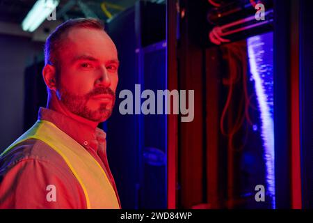 concentrated good looking technician in safety vest posing and looking at camera, date center Stock Photo