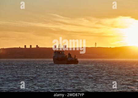 Silhouette of Supply vessel going in port during sunset on the horizon Stock Photo