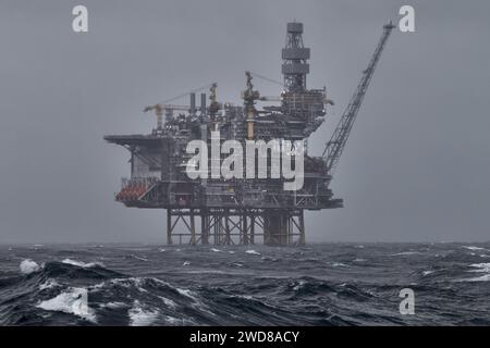 Offshore oil and gas platform in the sea, during storm, with grey sky and waves on the foreground. Stock Photo