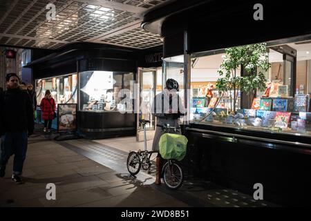 A Commuter stands with her Brompton folding bike outside a branch of Waterstones at Piccadilly on a cold winters evening in London, UK Stock Photo